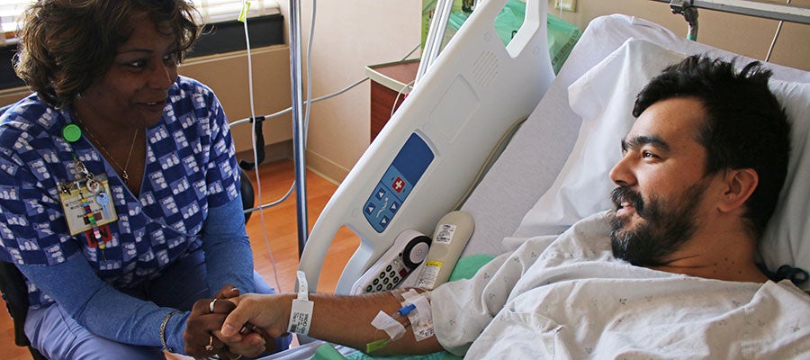 Medical staff next to a person in an hospital bed - comforting the person holding hands