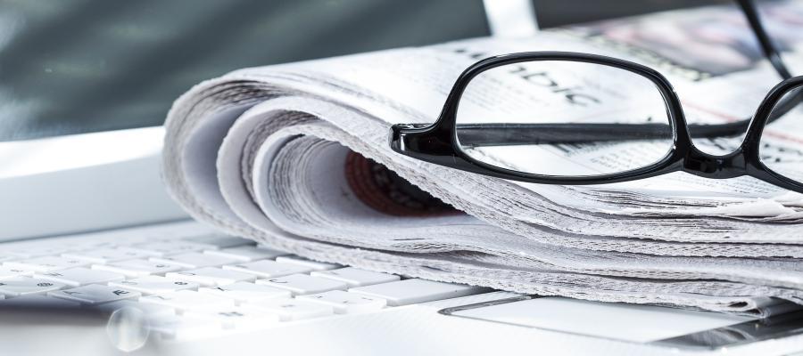 Eyeglasses sit on a folded newspaper on top of a laptop keyboard.